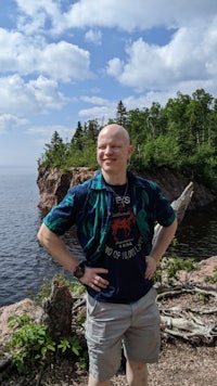 a bald man standing in front of a body of water